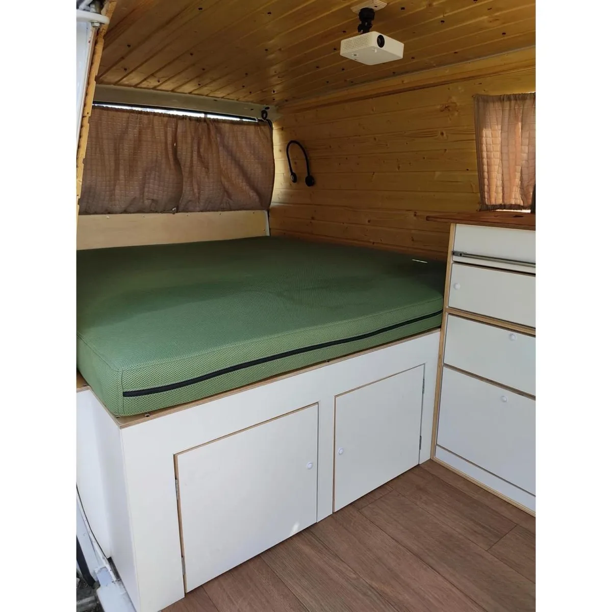 Bed with green mattress, ceiling-mounted projector and front cabin in the background