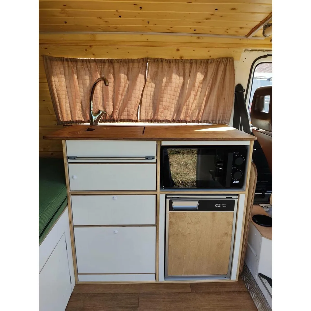 Kitchen with wooden countertop, microwave, fridge and caramel-tone curtain