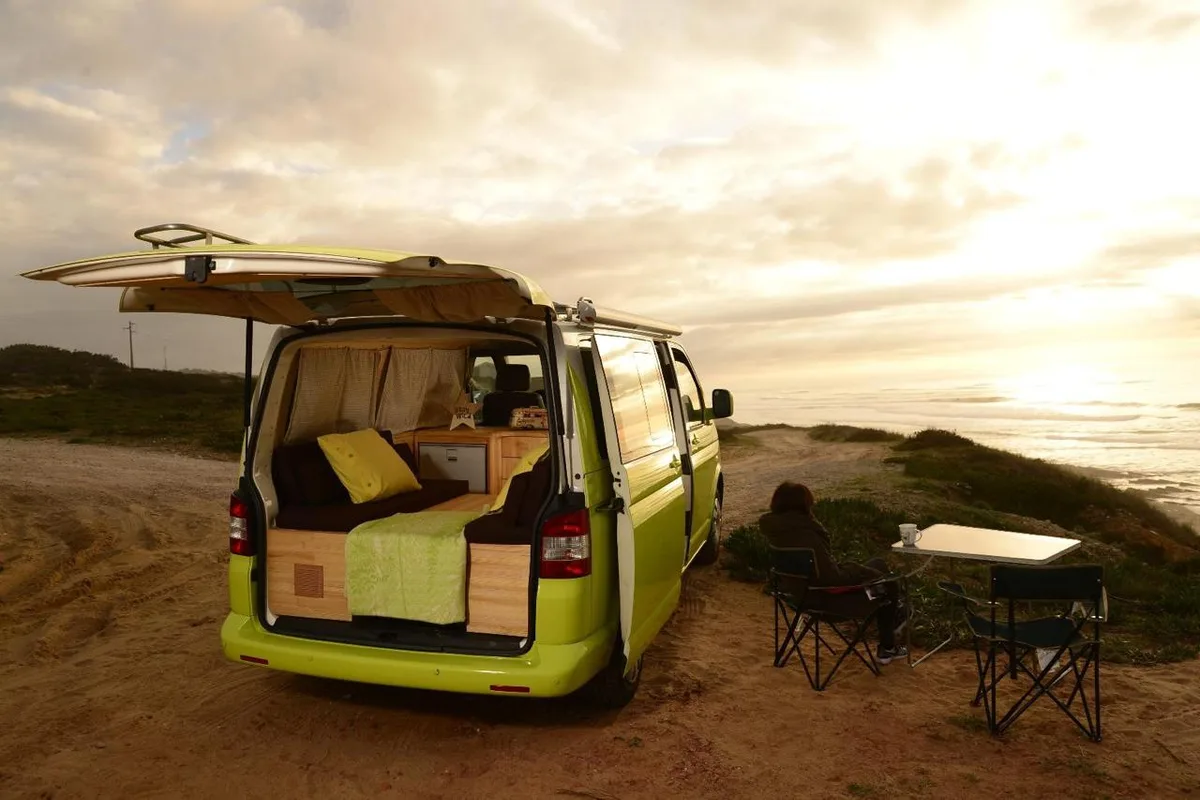 Green VW T5 at sunset beach, open rear door with bed