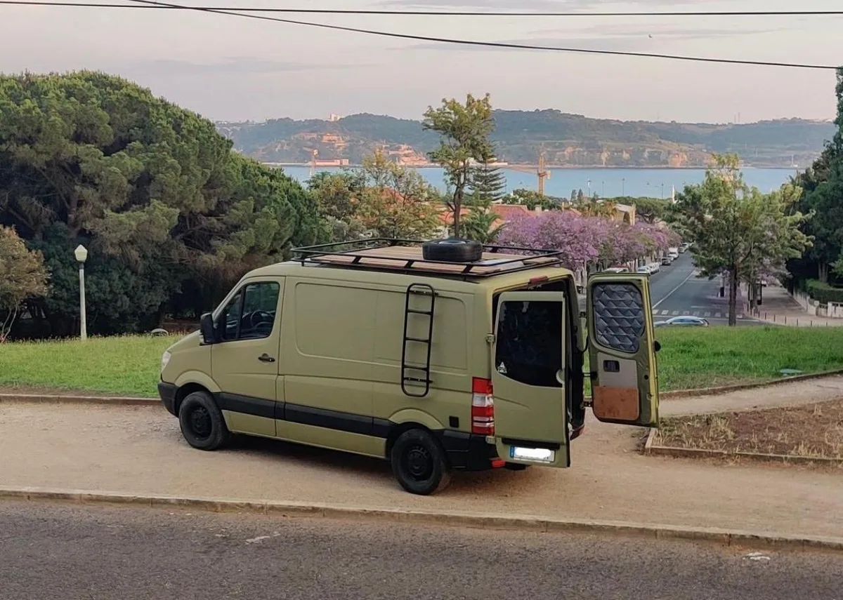 Military green Mercedes Sprinter with roof deck and ladder, Lisbon in the background
